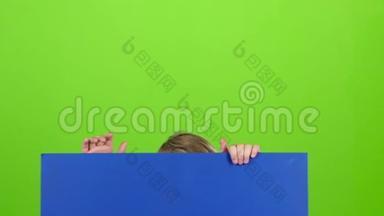 小男孩从一张<strong>蓝色海报</strong>后面出现，看着他再次躲藏起来。 绿色屏幕。 慢动作